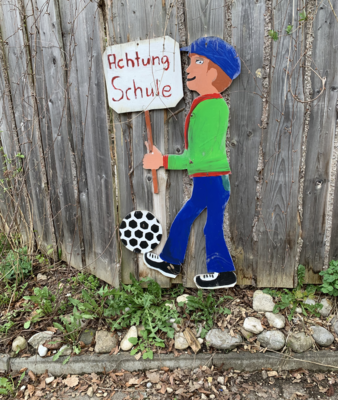 Figur mit Schild "Achtung Schule" an einem Zaun | © Stadt Geretsried