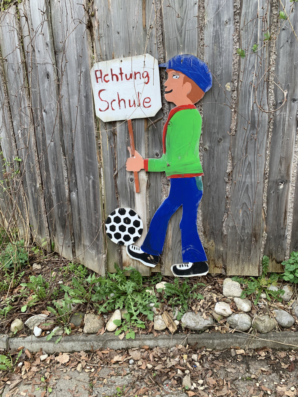 Bemalte Holzfigur mit einem Schild, auf dem Achtung Schule zu lesen ist  | © Stadt Geretsried