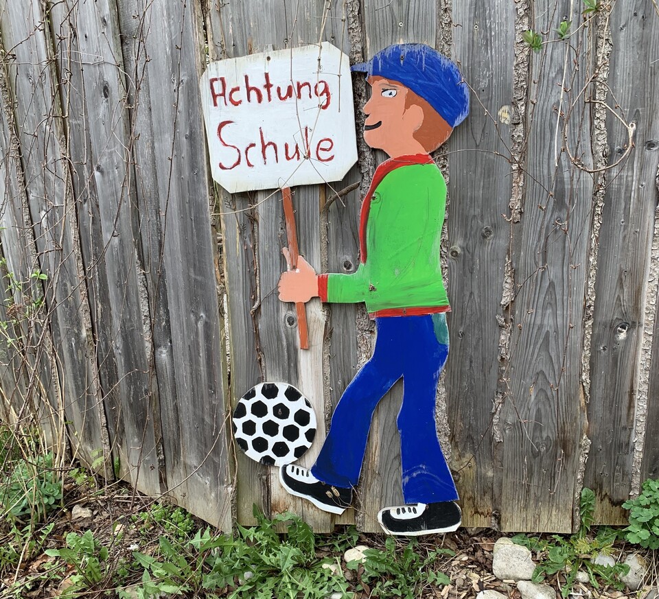 Bemalte Holzfigur mit einem Schild, auf dem Achtung Schule zu lesen ist  | © Stadt Geretsried