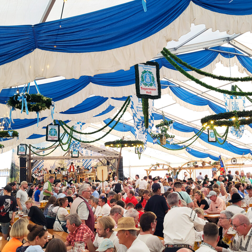 Blick ins vollbesetzte Festzelt mit Bühne und blau-weißer Dekoration | © Stadt Geretsried